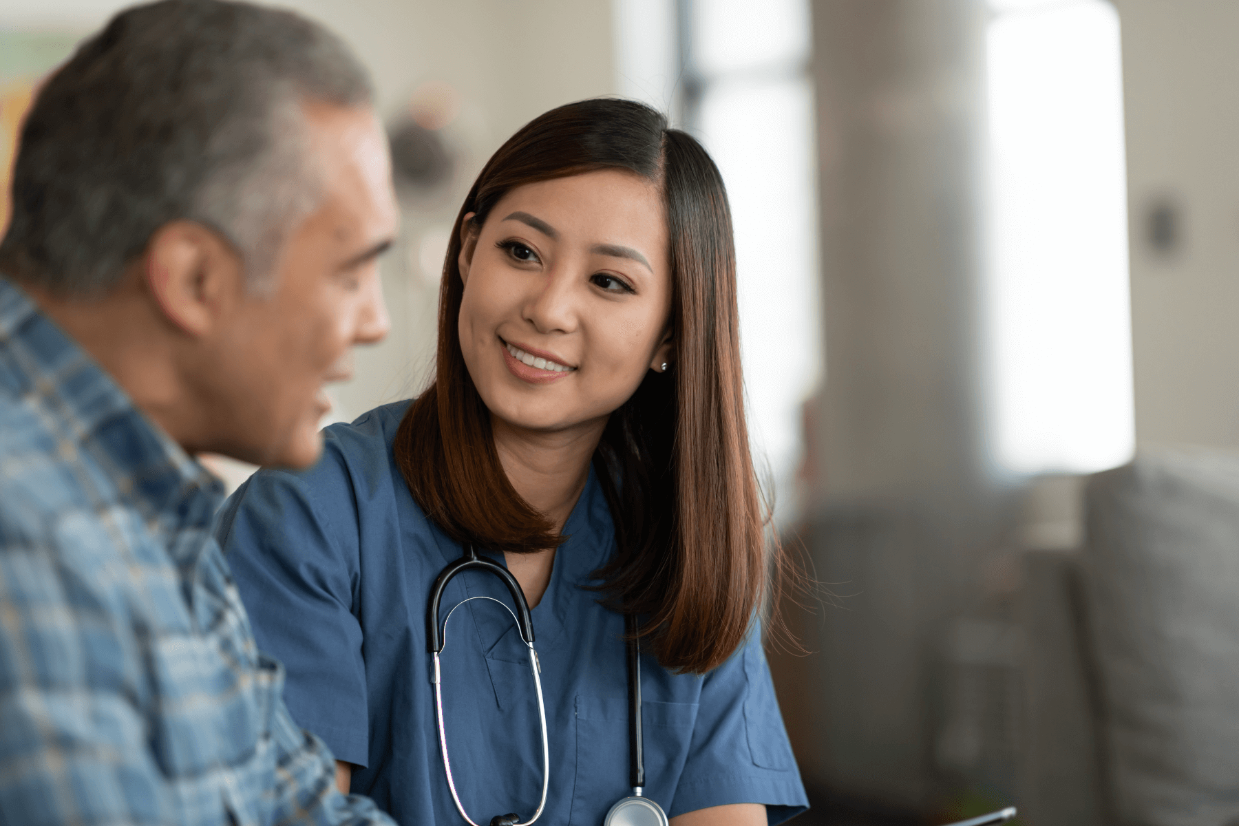 A nurse is talking to an older man in a living room.