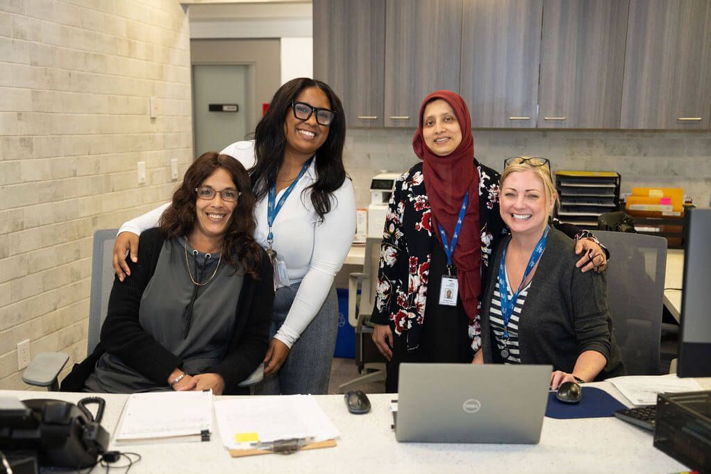A group of women are posing for a picture in front of a laptop computer.