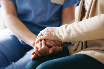 A nurse is holding the hands of an elderly woman.