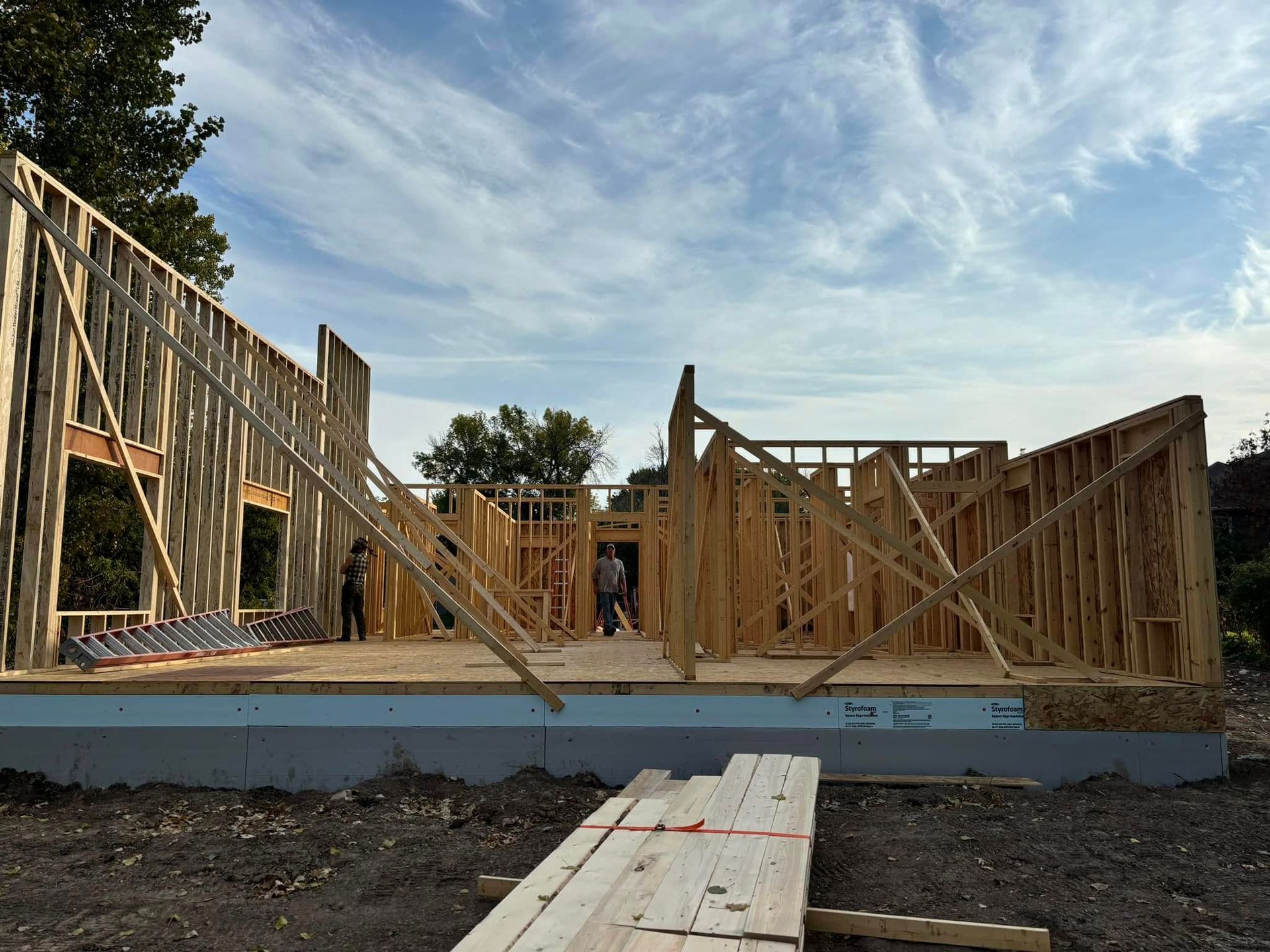 Framed wooden structure of a house under construction, against a cloudy sky.