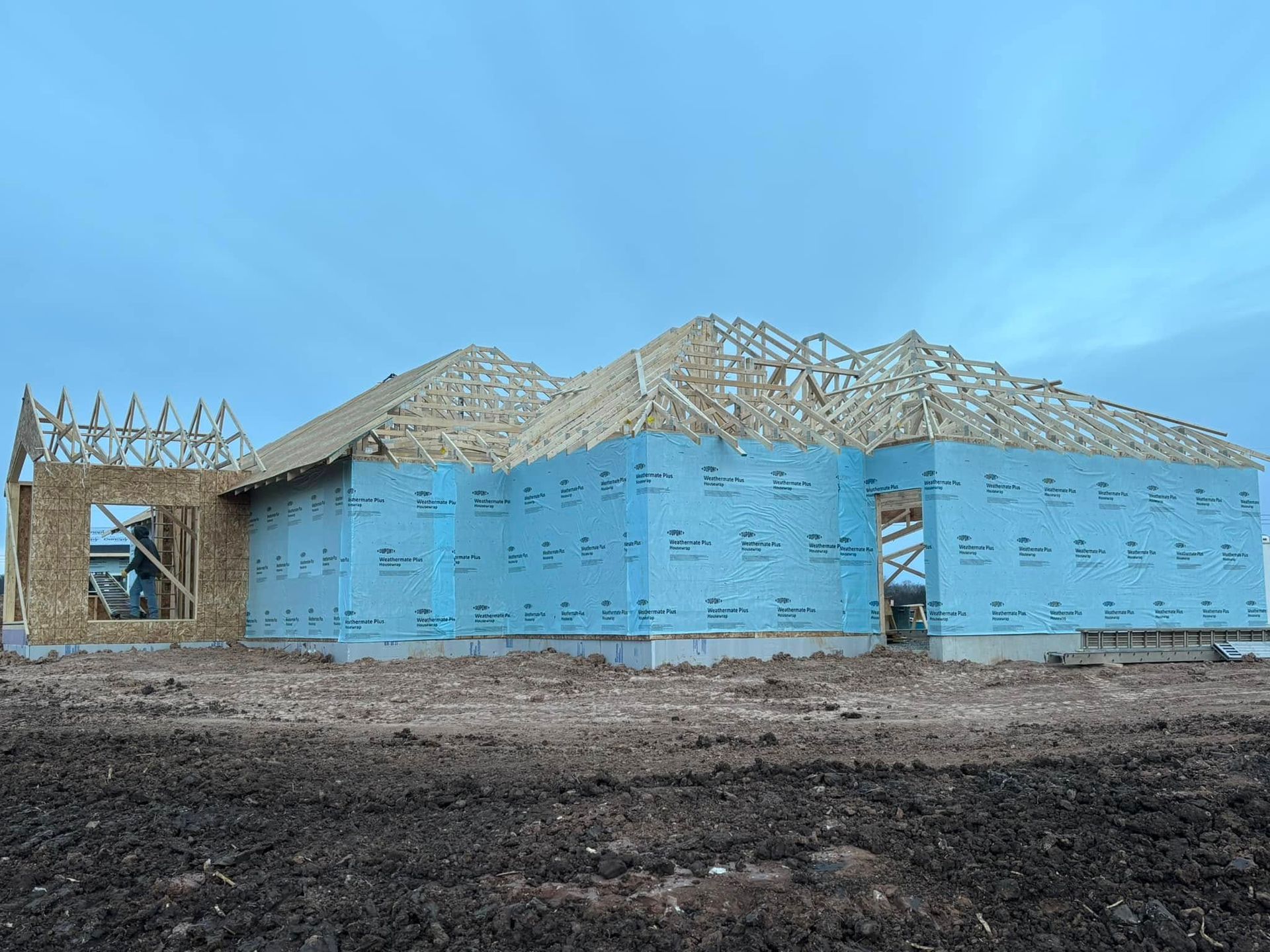 House under construction; blue sheathing, exposed wood framing, overcast sky.