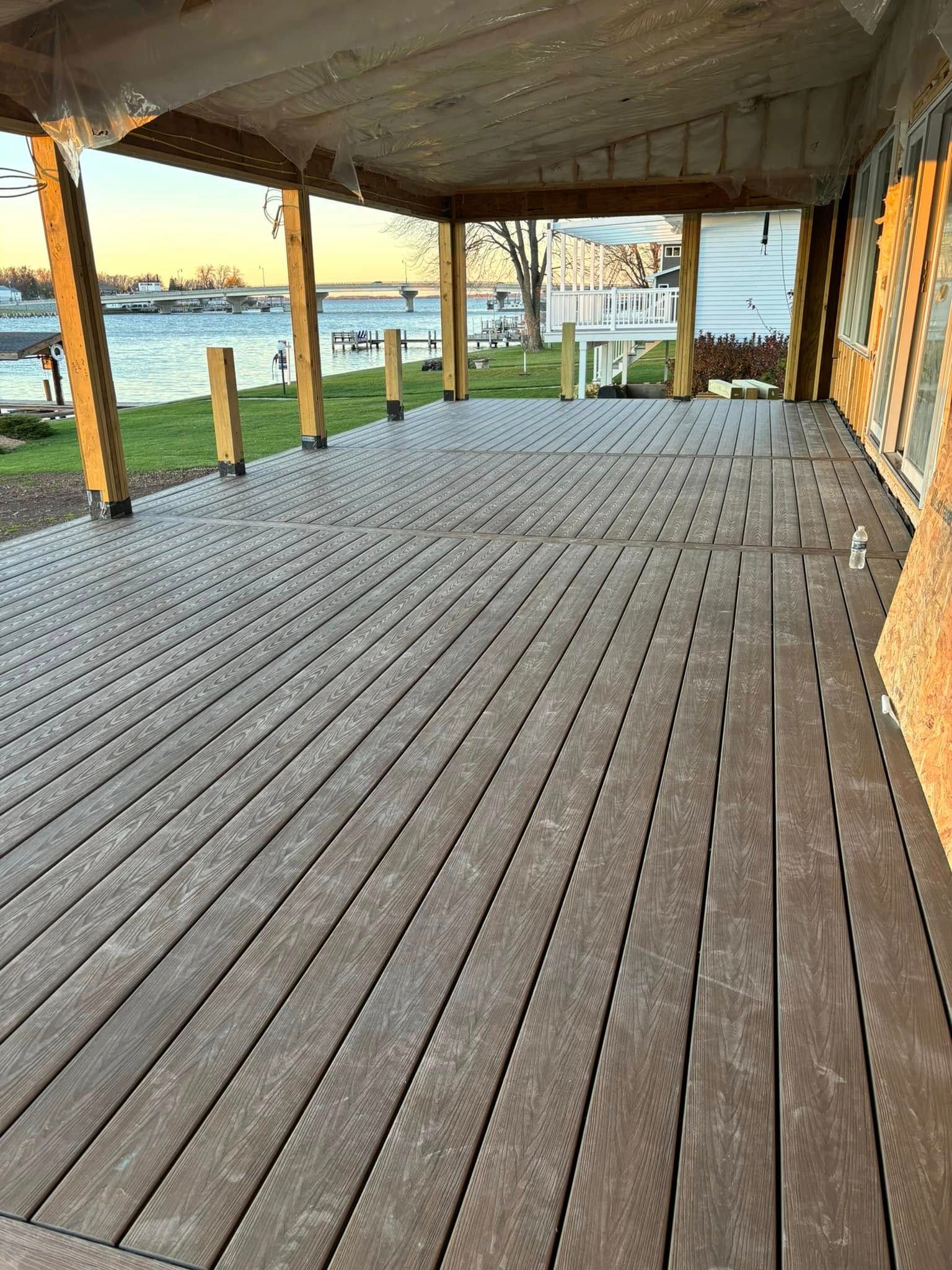 Covered deck with composite flooring, overlooking water. Wooden posts support the roof.