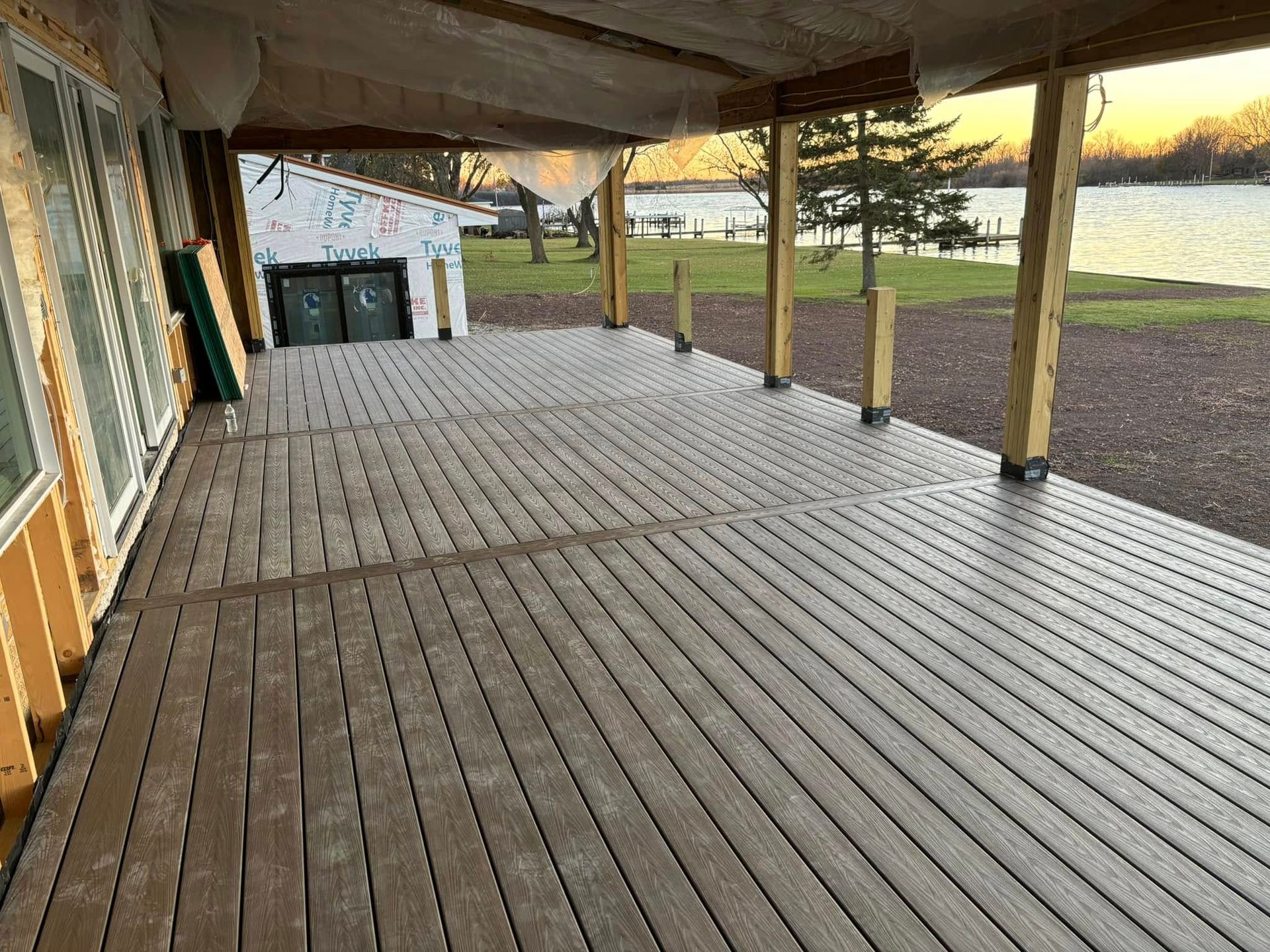 A wide, brown deck with a view of a lake. Partially constructed, with some building materials visible.
