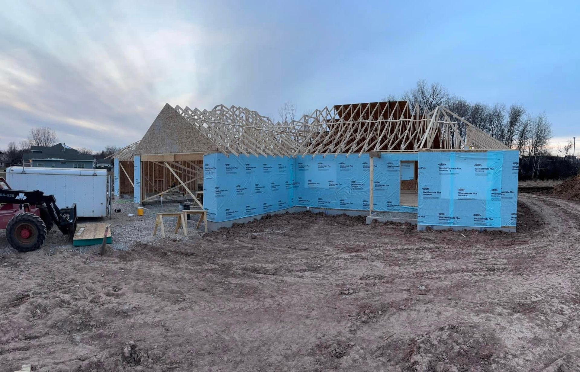 Construction site: a house frame with blue insulation, under a cloudy sky.