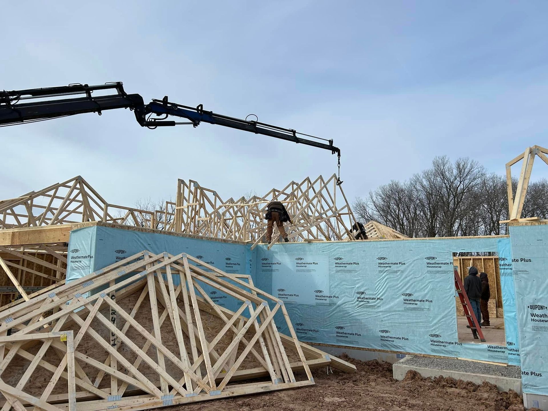Construction workers on a building site, erecting wooden roof trusses. Blue insulation covers the walls.