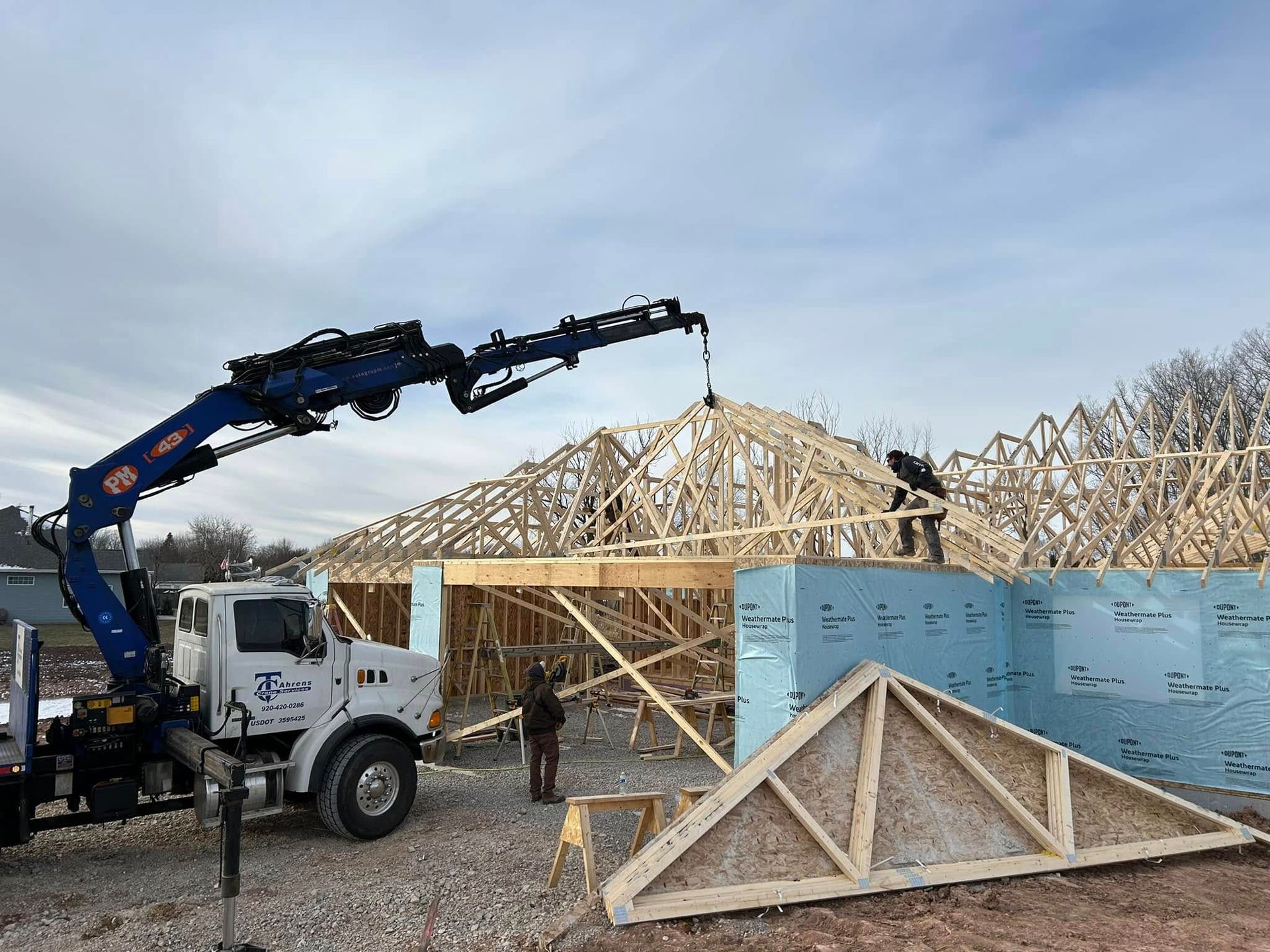 Crane lifting wooden trusses onto a building frame, construction site.