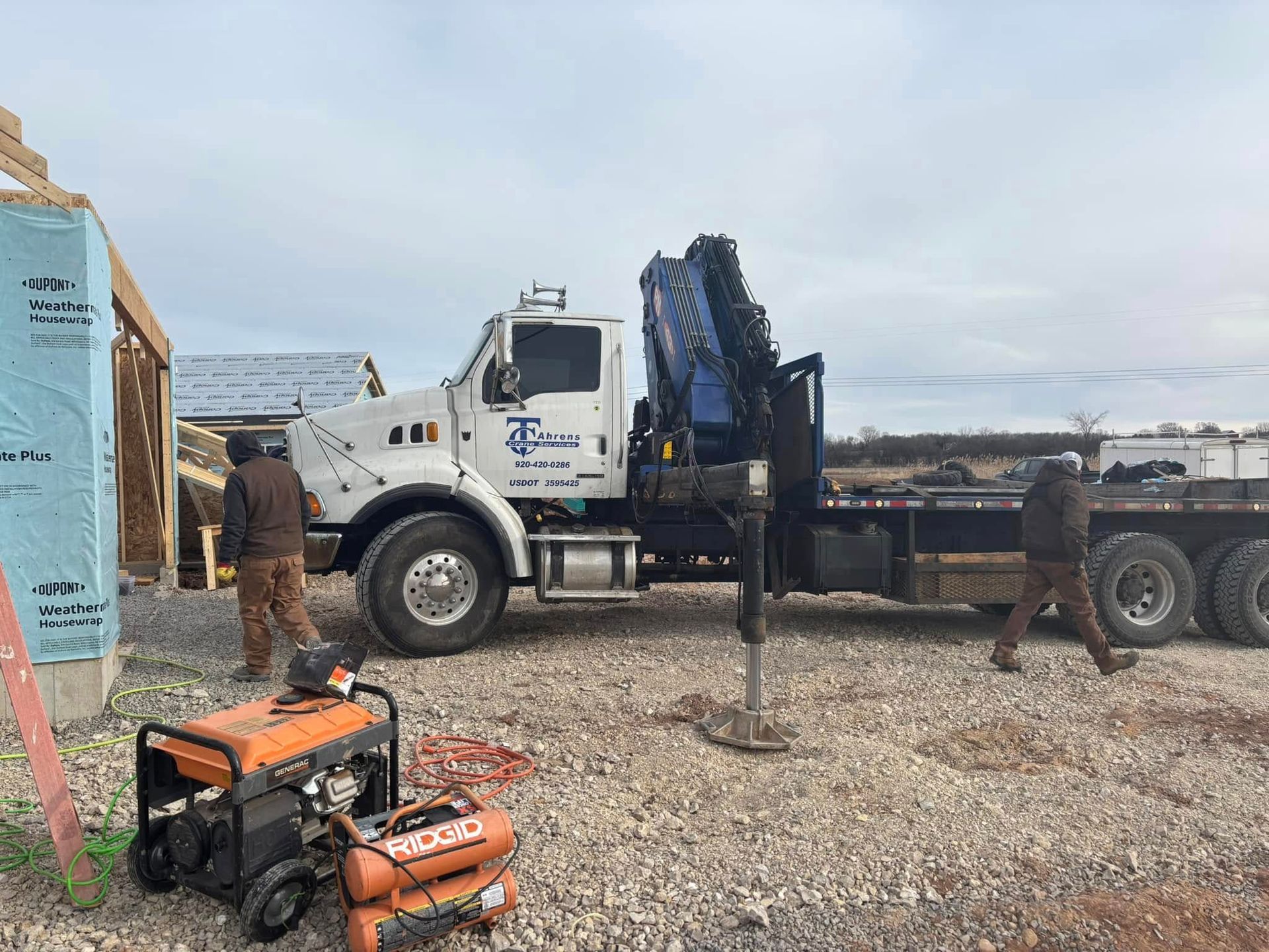Construction site with a crane truck and workers; orange air compressor in foreground.