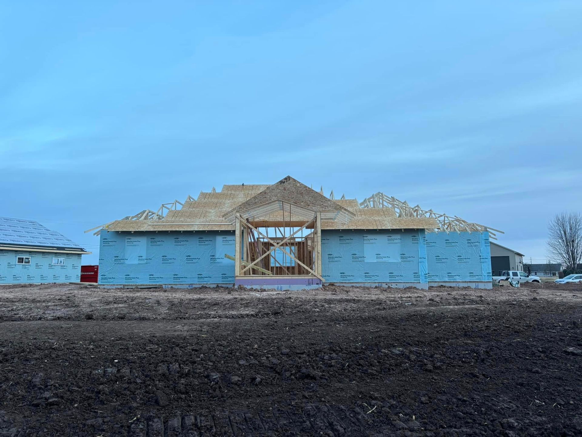 House under construction, wood framing, blue sheathing, overcast sky.