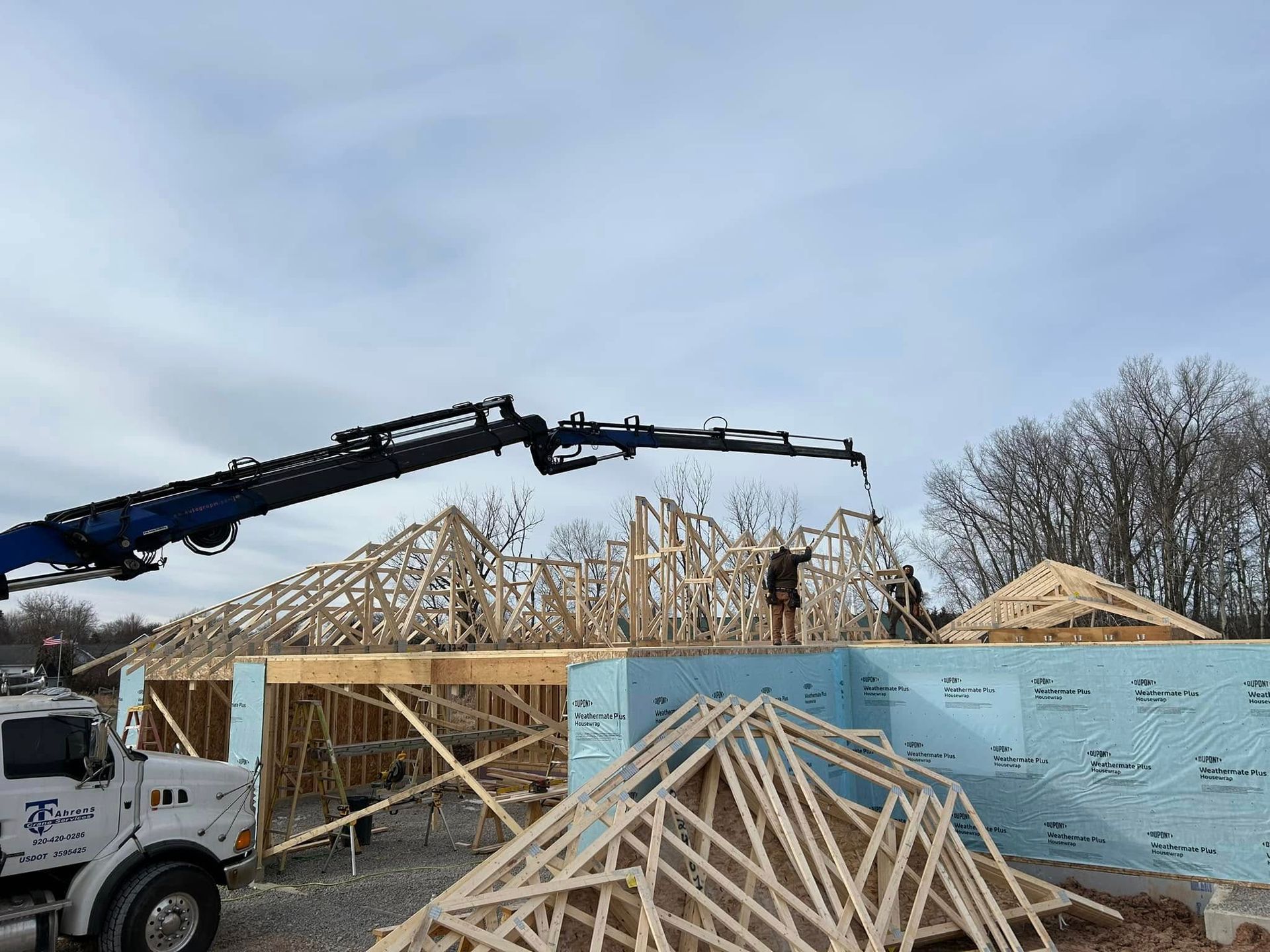 A crane lifts roof trusses during the construction of a building on a cloudy day.