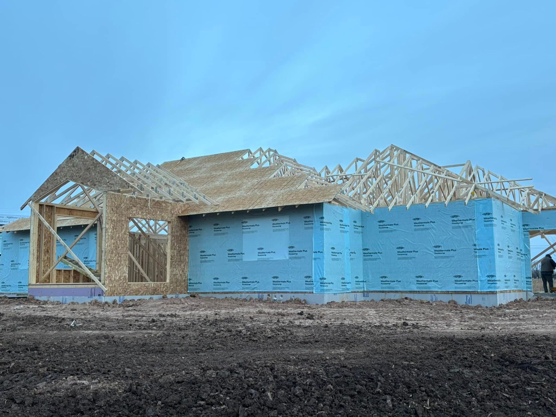 House under construction, blue siding, wooden frame, cloudy sky, dirt.