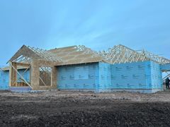 House under construction, blue siding, wooden frame, cloudy sky, dirt.