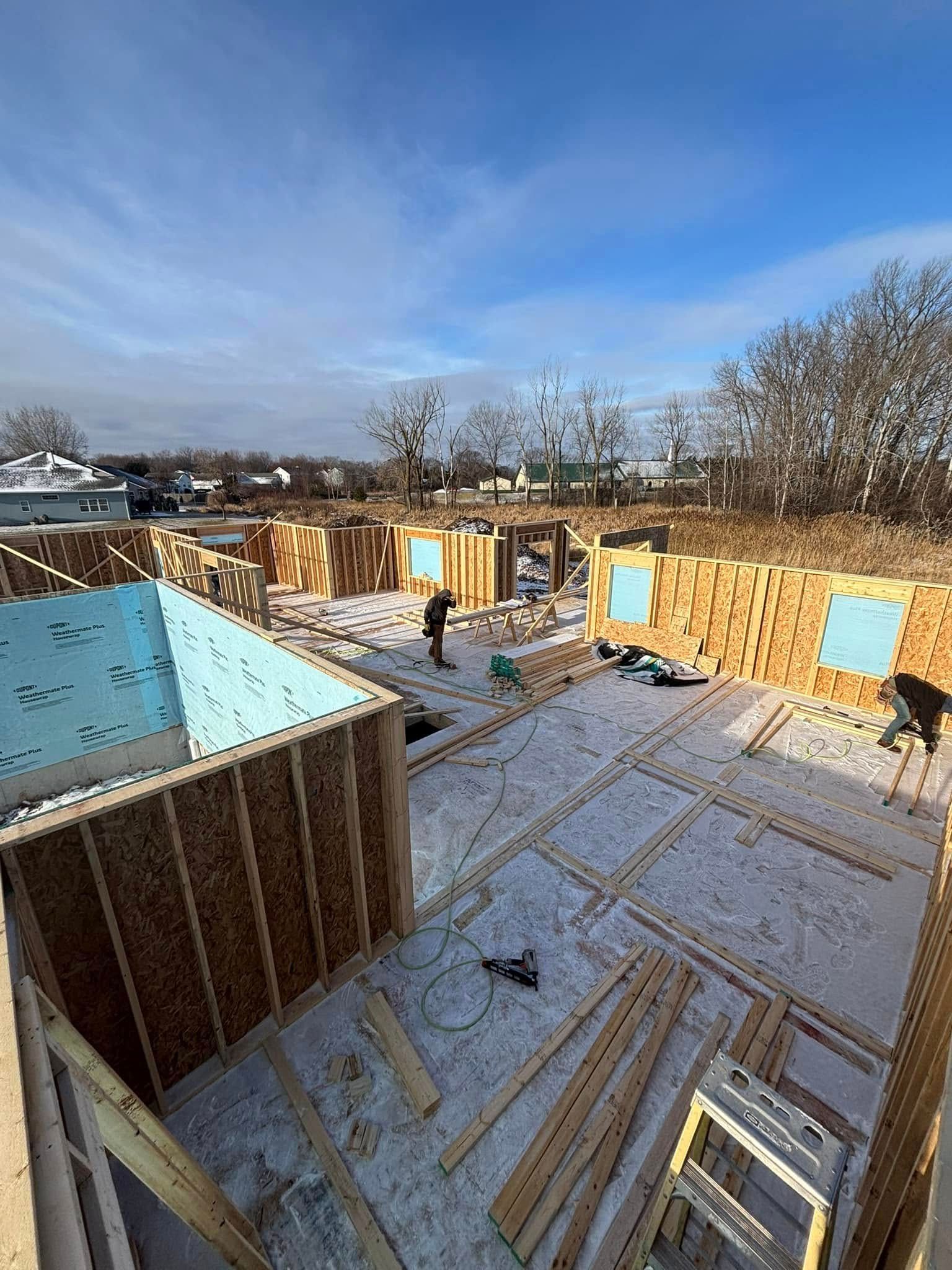 Construction site with wooden framing and workers on a snowy day under a blue sky.