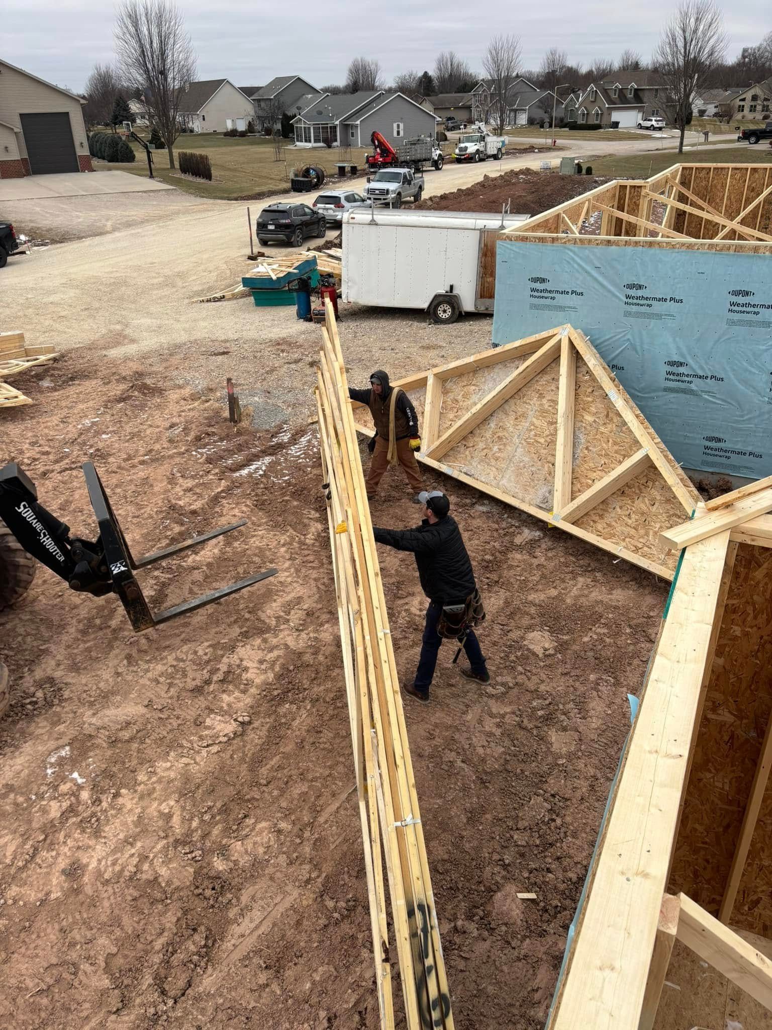 Construction workers installing a wall on a building site. Forklift nearby, houses in the background.