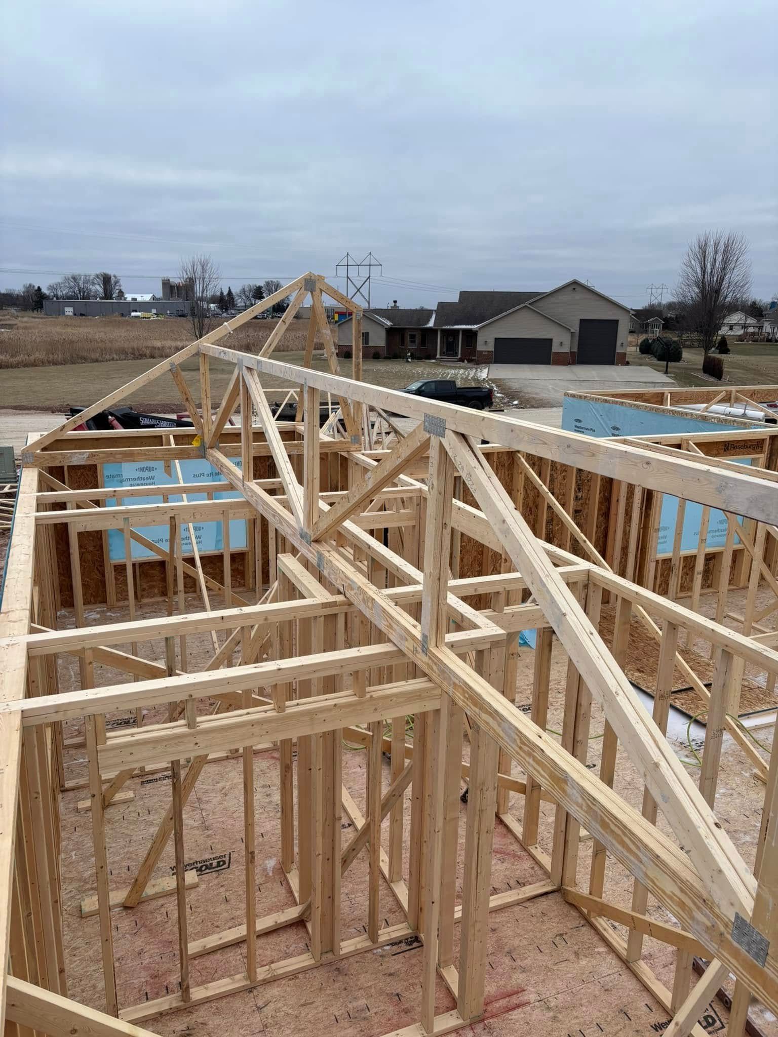 Wooden house frame under construction, featuring trusses, studs, and insulation; cloudy day.