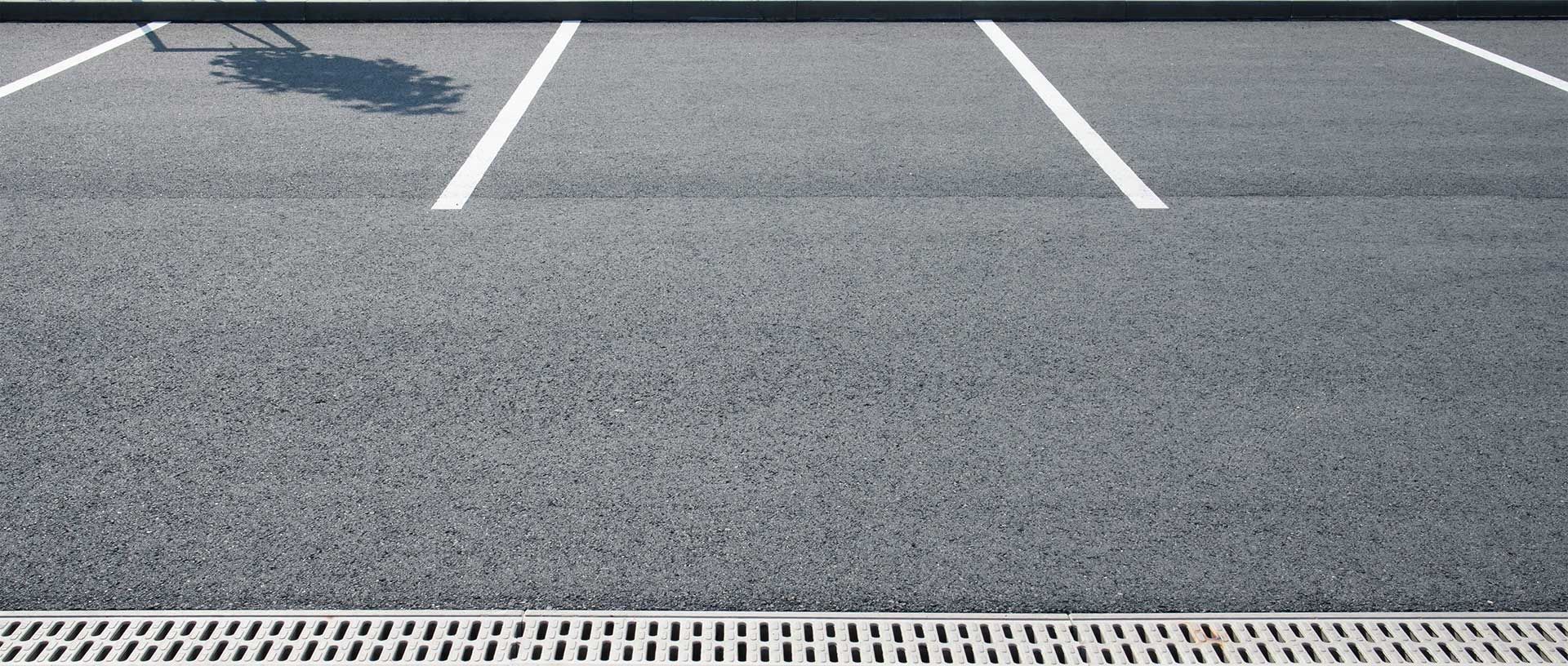 Empty parking spaces with white painted lines on asphalt pavement, adjacent to a metal drainage grate.