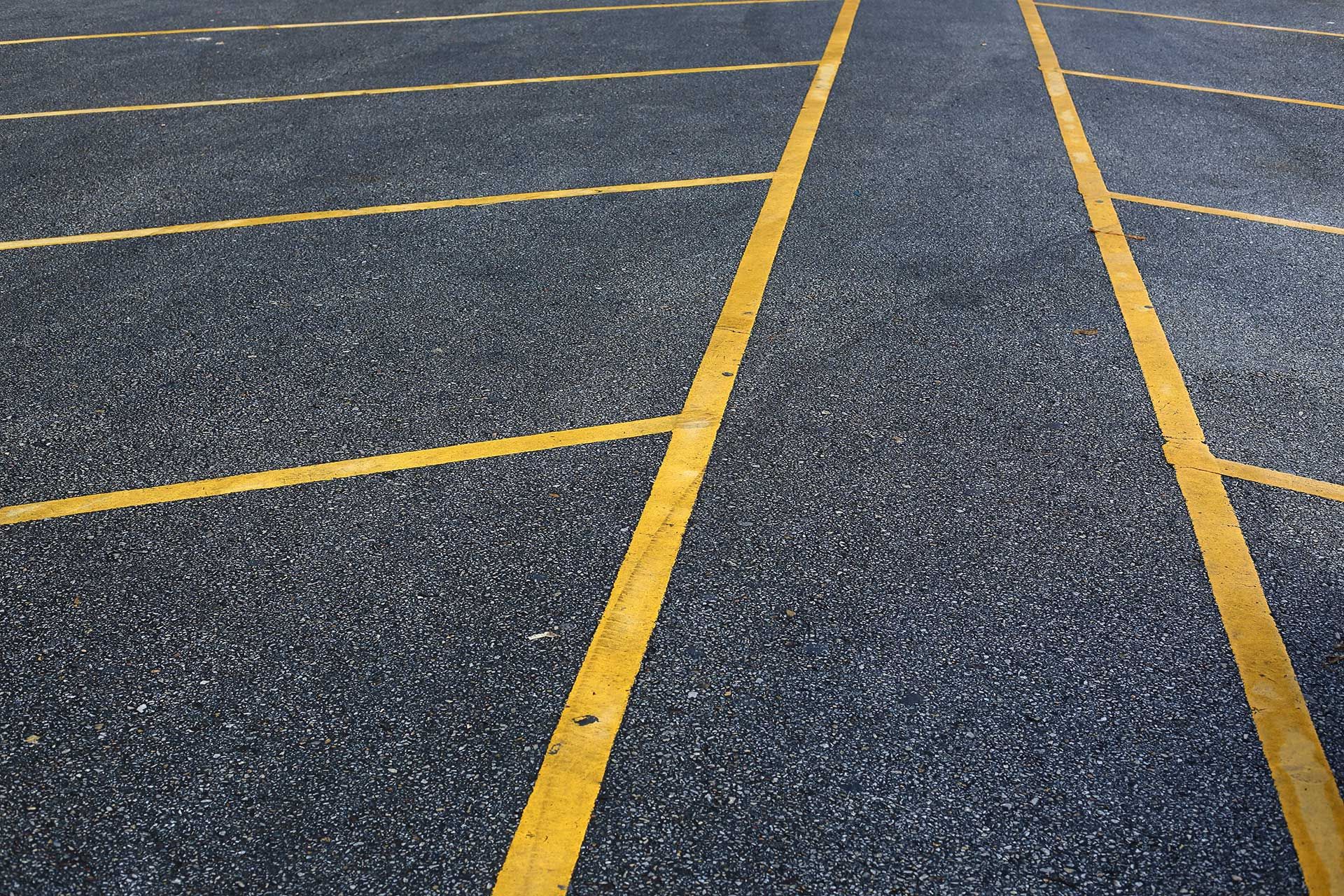 A high-angle view of an empty asphalt parking lot with yellow-painted parking space markings.