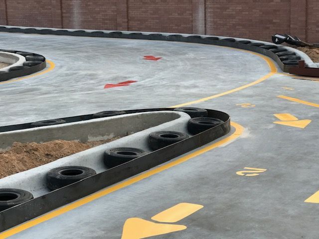 Concrete go-kart track with tire barriers, painted yellow lane markings, and directional arrows on the ground.