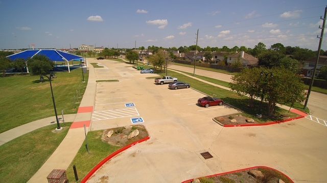 An aerial view of a mostly empty parking lot with red-painted curbs, a blue shade structure, and a paved walkway.
