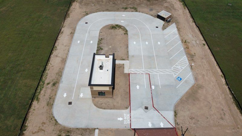 An aerial view of a concrete drive-through facility with marked lanes, a small building, and a handicap parking space.