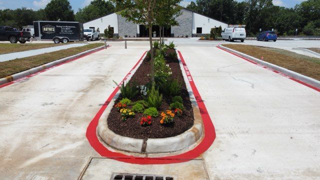 A parking lot entrance with a central landscaped island outlined in red paint, with a building in the background.