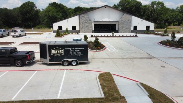 A black truck pulling a Haynes trailer parked in a lot in front of a modern, white building with stone accents.