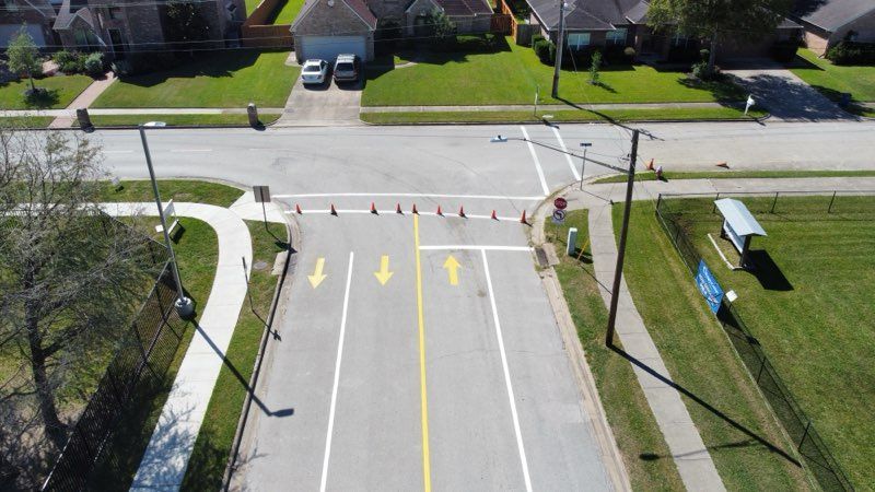 An aerial view of a three-lane street ending at a T-intersection, blocked by a row of orange traffic cones.