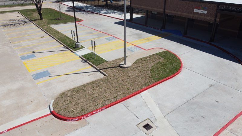 An aerial view of an outdoor parking area with a central landscaped island outlined by a red curb.