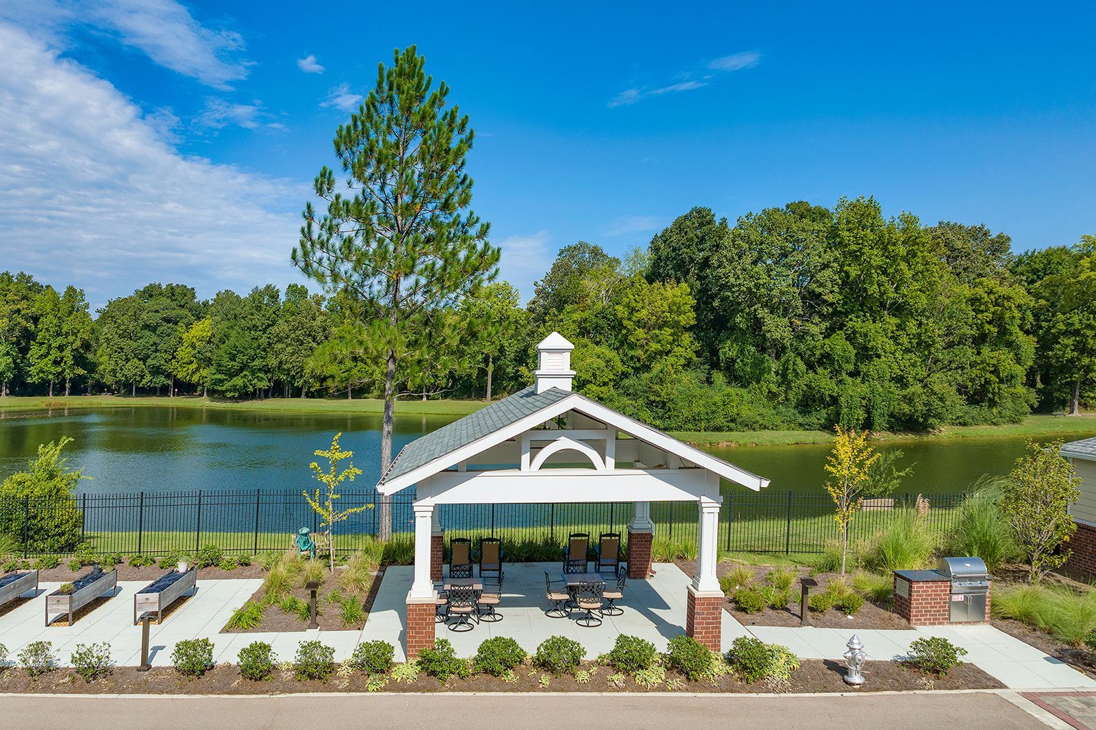 Pavilion near a lake, with seating, surrounded by trees under a blue sky.