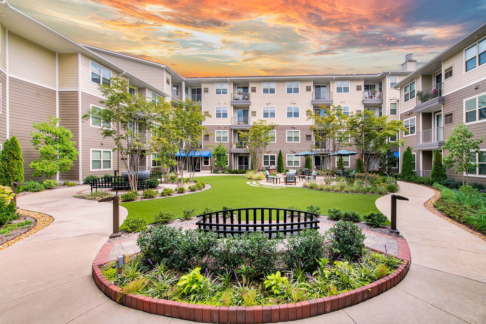 Courtyard with lawn, landscaping, benches, and multi-story building at sunset.