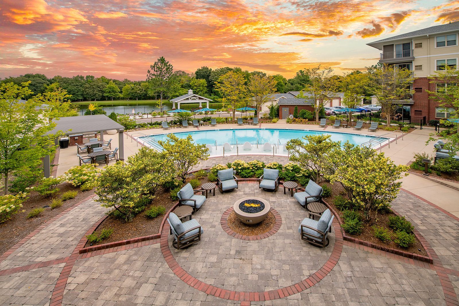 A resort scene with a pool, fire pit, lake, and setting sun.