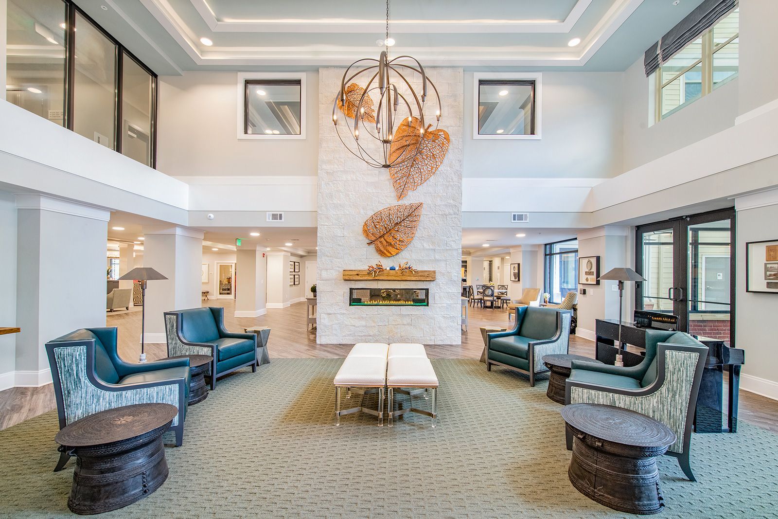 A spacious lobby with teal armchairs, a fireplace, and decorative sculpture; natural light.