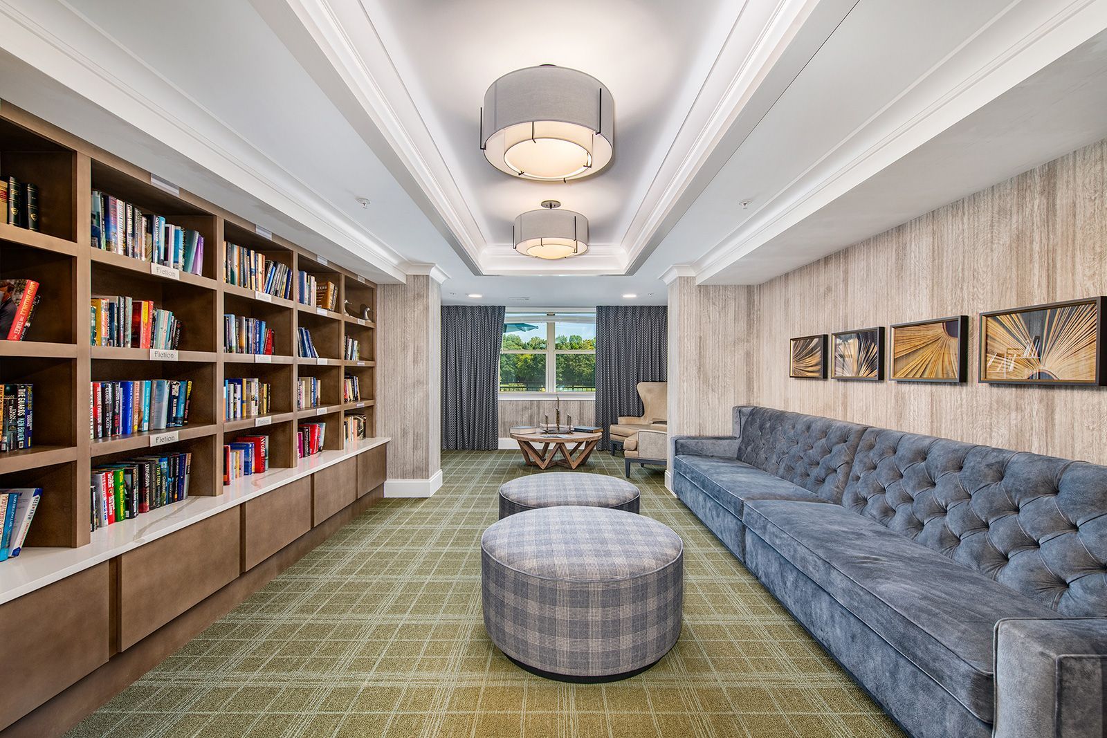 Library lounge with built-in bookshelves, gray sofa, patterned ottomans, and decorative ceiling lights.