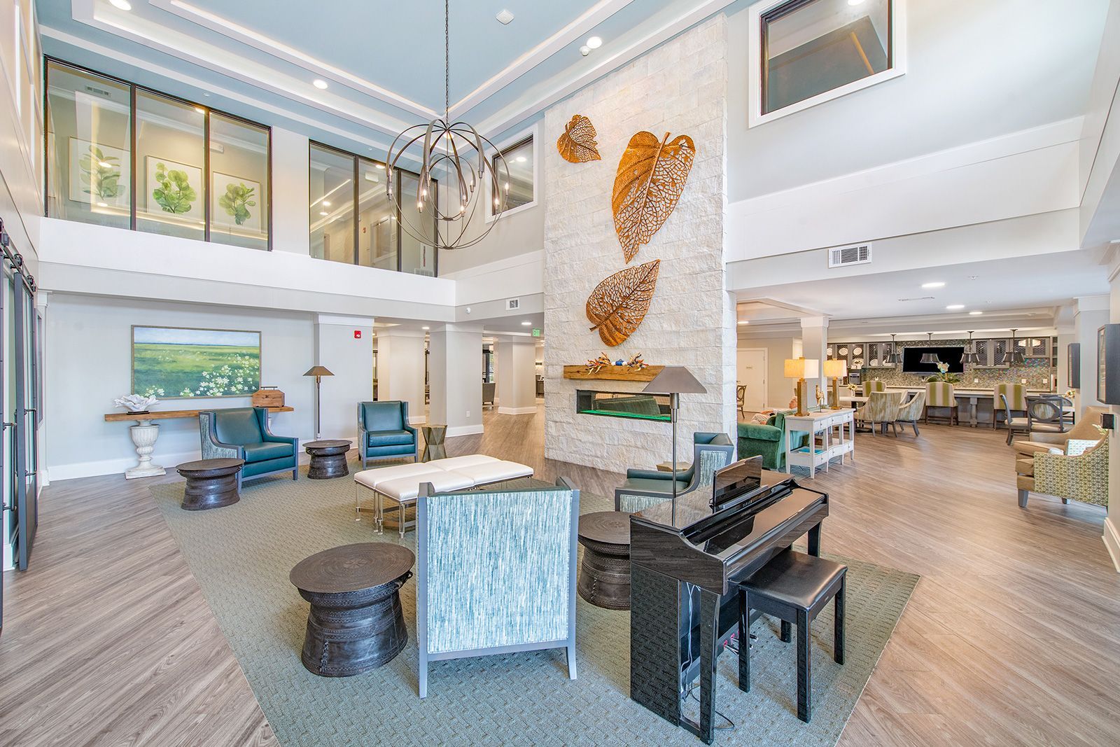 Spacious lobby with a piano, fireplace, seating areas, and decorative art. Bright and airy with neutral tones.