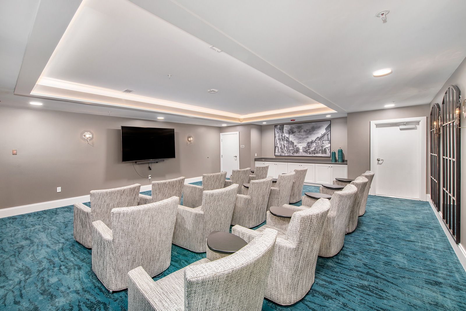 Movie theater with blue carpet, white chairs, large TV, and a decorative wall.