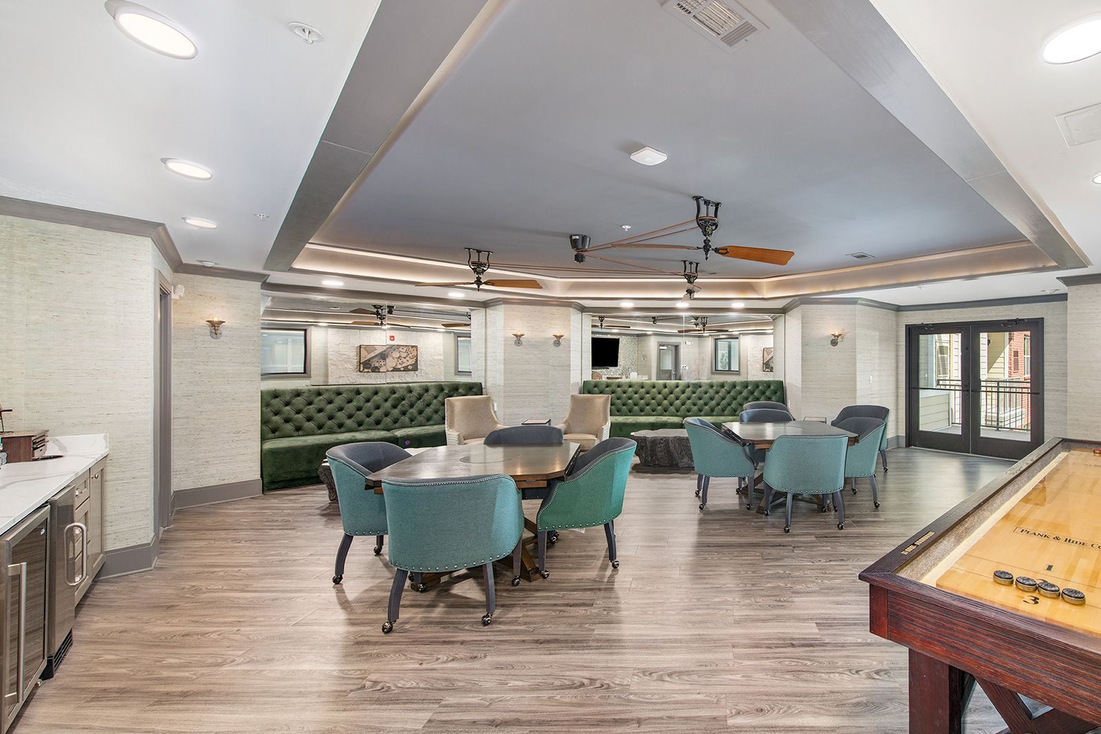 Game room with teal chairs, round tables, green velvet seating, and shuffleboard.