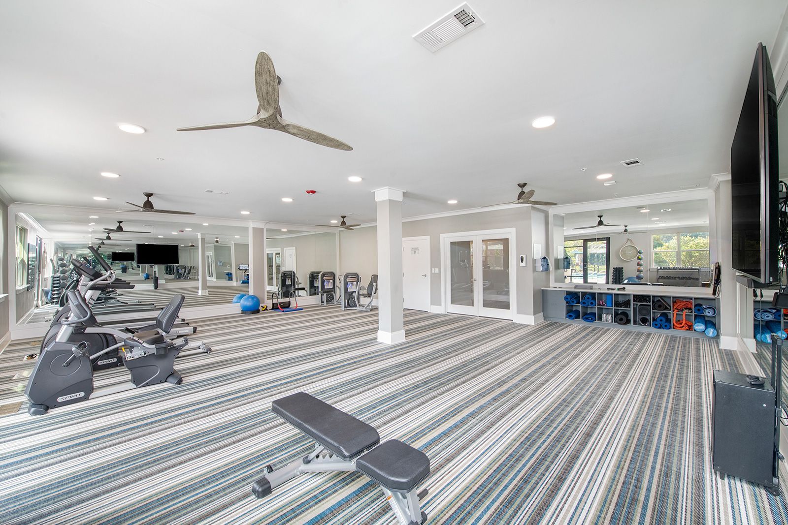 Gym with various workout machines, large mirrors, and a bench, with blue and grey striped carpet.