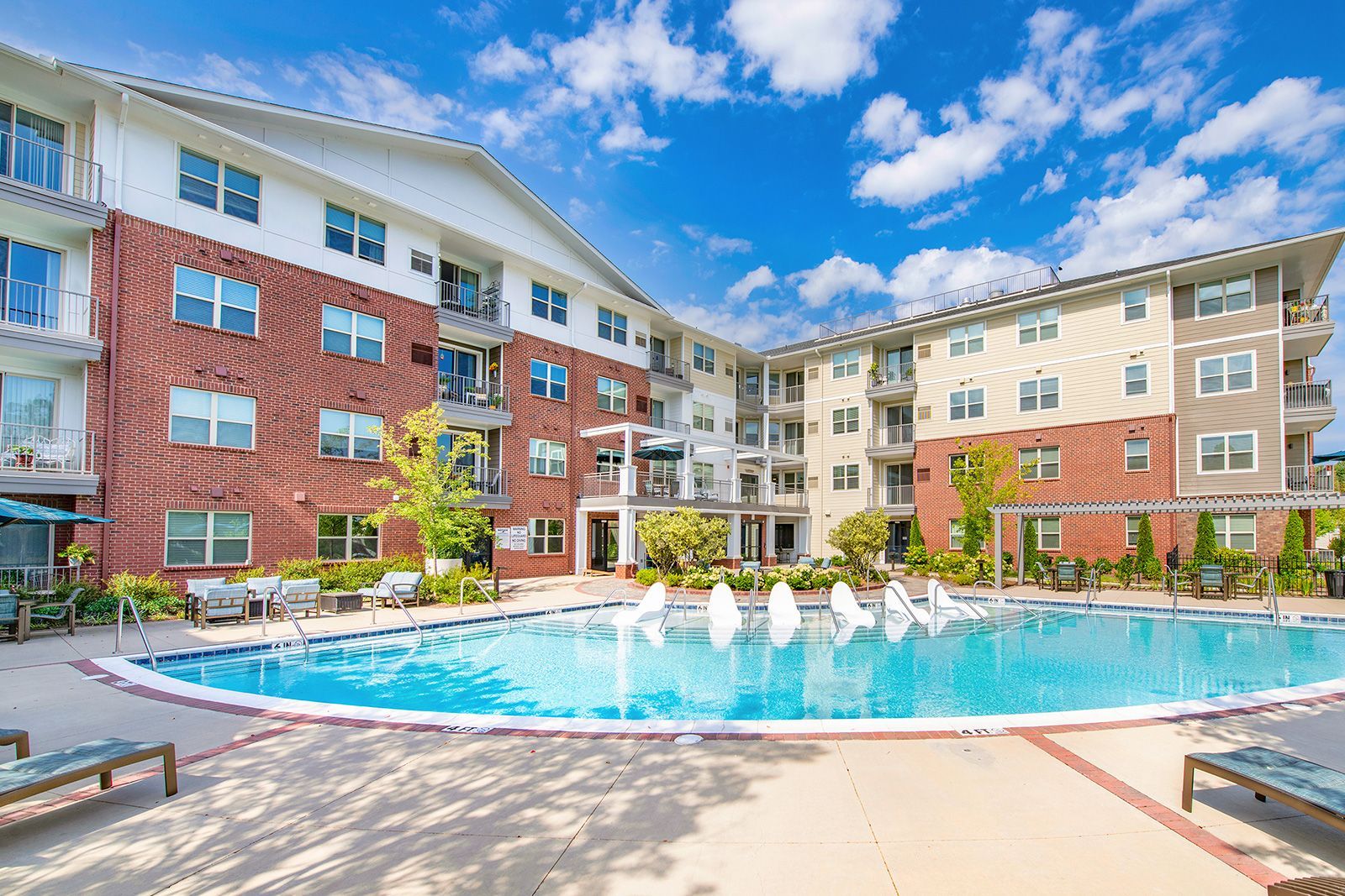 Apartment complex with pool; blue sky, brick facade, lounge chairs.