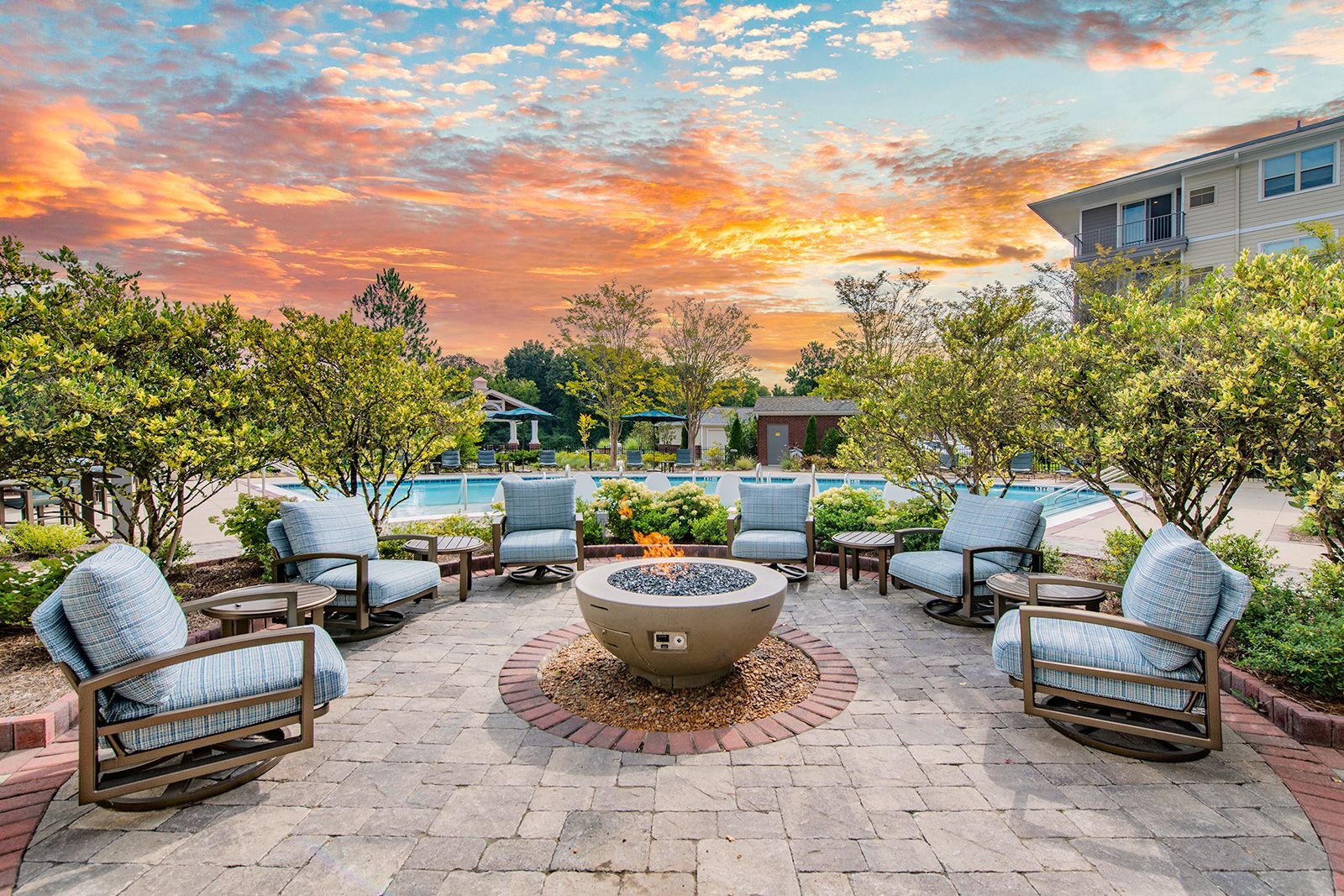 Outdoor seating area around a fire pit with chairs, a pool, and sunset sky.