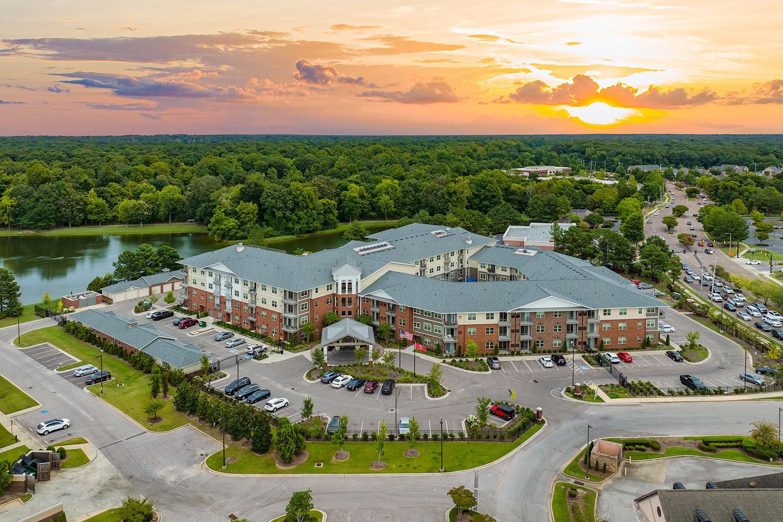 Large senior living facility at sunset, with a lake and trees surrounding it.