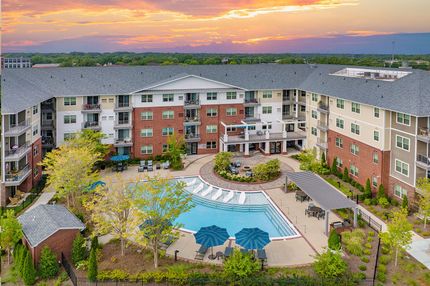 Aerial view of apartment complex with pool and colorful sunset. Brick and beige buildings surround a pool with umbrellas.