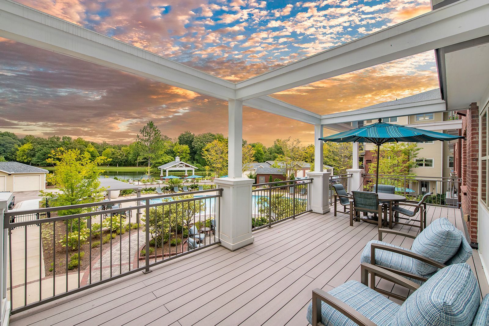 A deck with outdoor furniture overlooking a pool and lake under a colorful sunset.