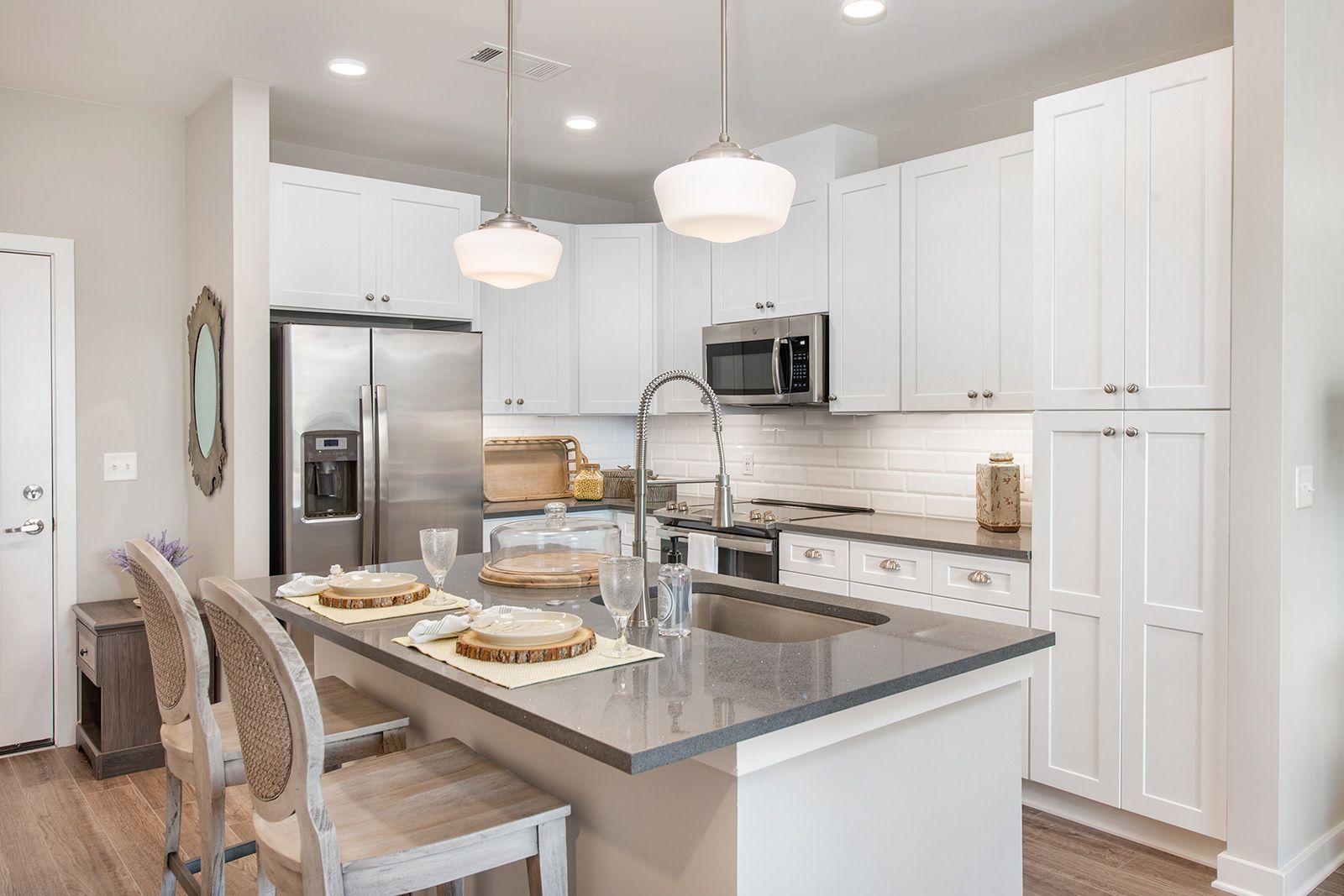 White kitchen with island, stainless steel appliances, and two pendant lights.