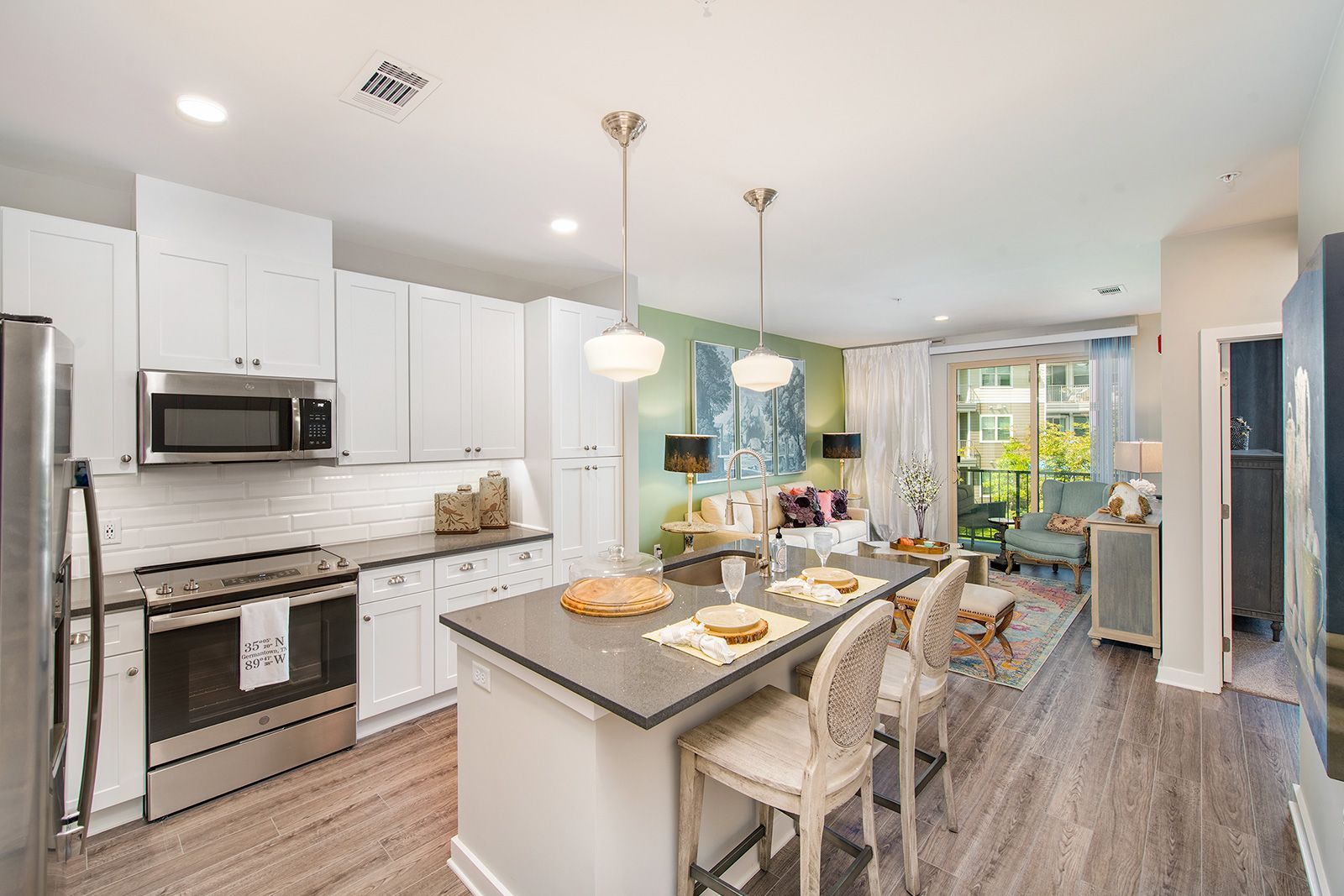 Modern kitchen with island, stainless steel appliances, open to living room with balcony view.