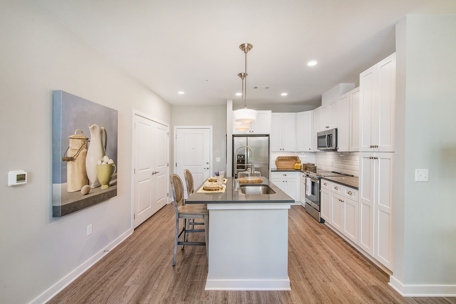 Modern kitchen with white cabinets, island, stainless steel appliances, and hardwood flooring.