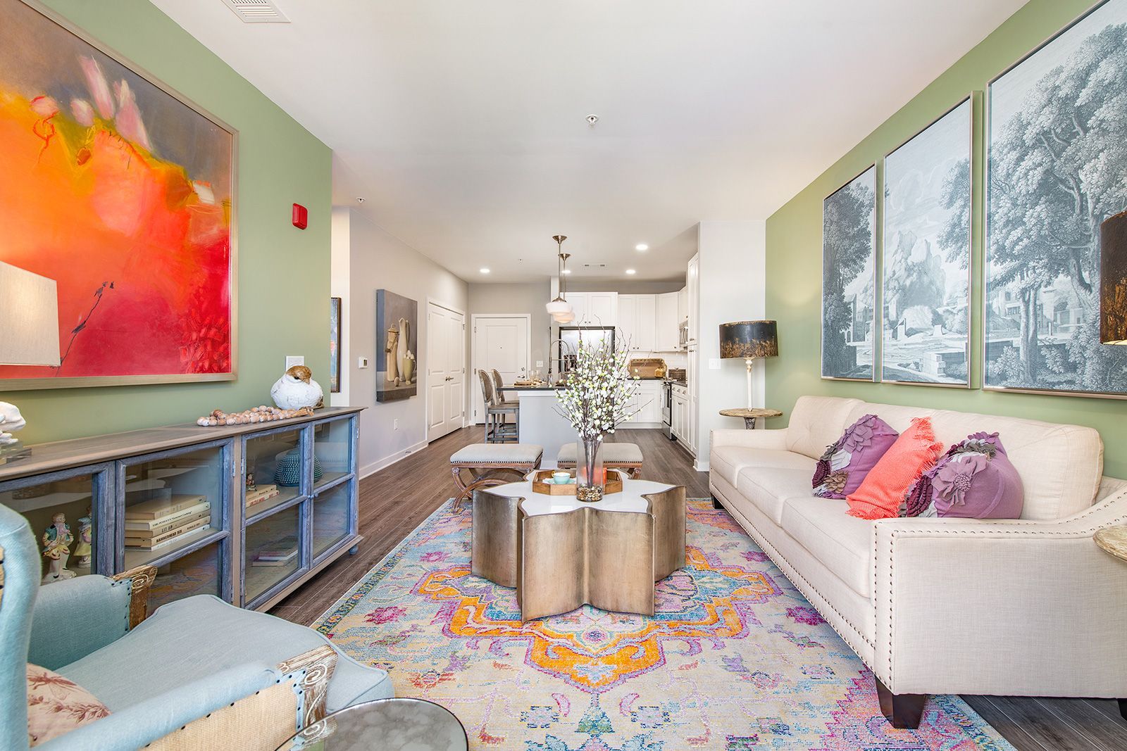 Living room with green walls, white sofa, gold table, colorful rug, and art.