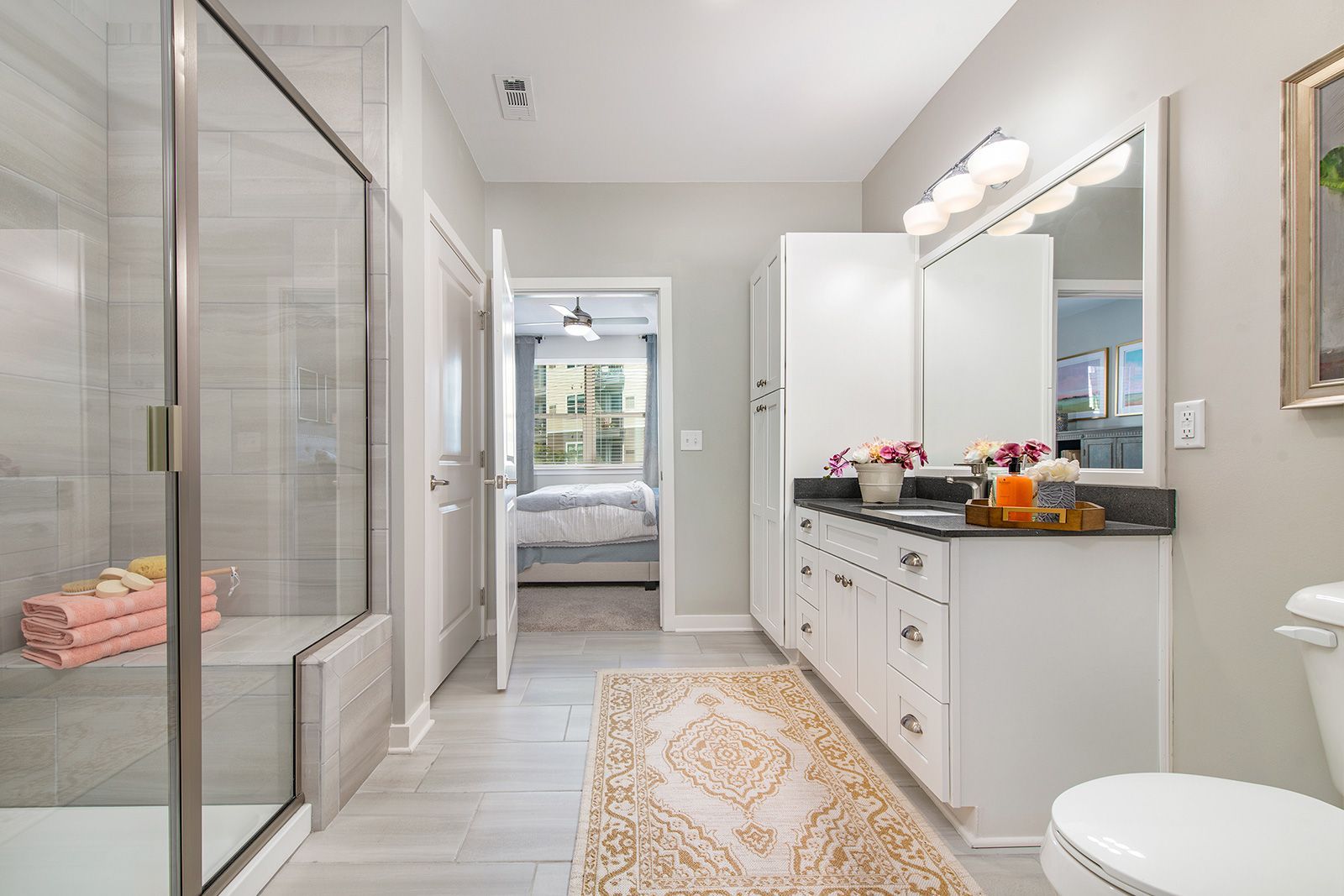 Bathroom with gray tile, white cabinets, and a doorway leading to a bedroom.