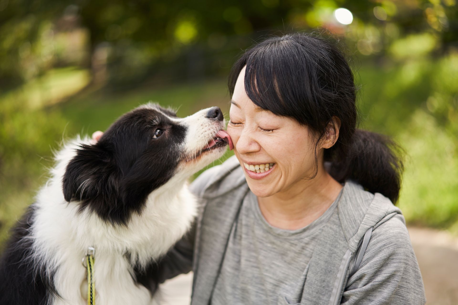Woman smiles as black and white dog licks her face outdoors.