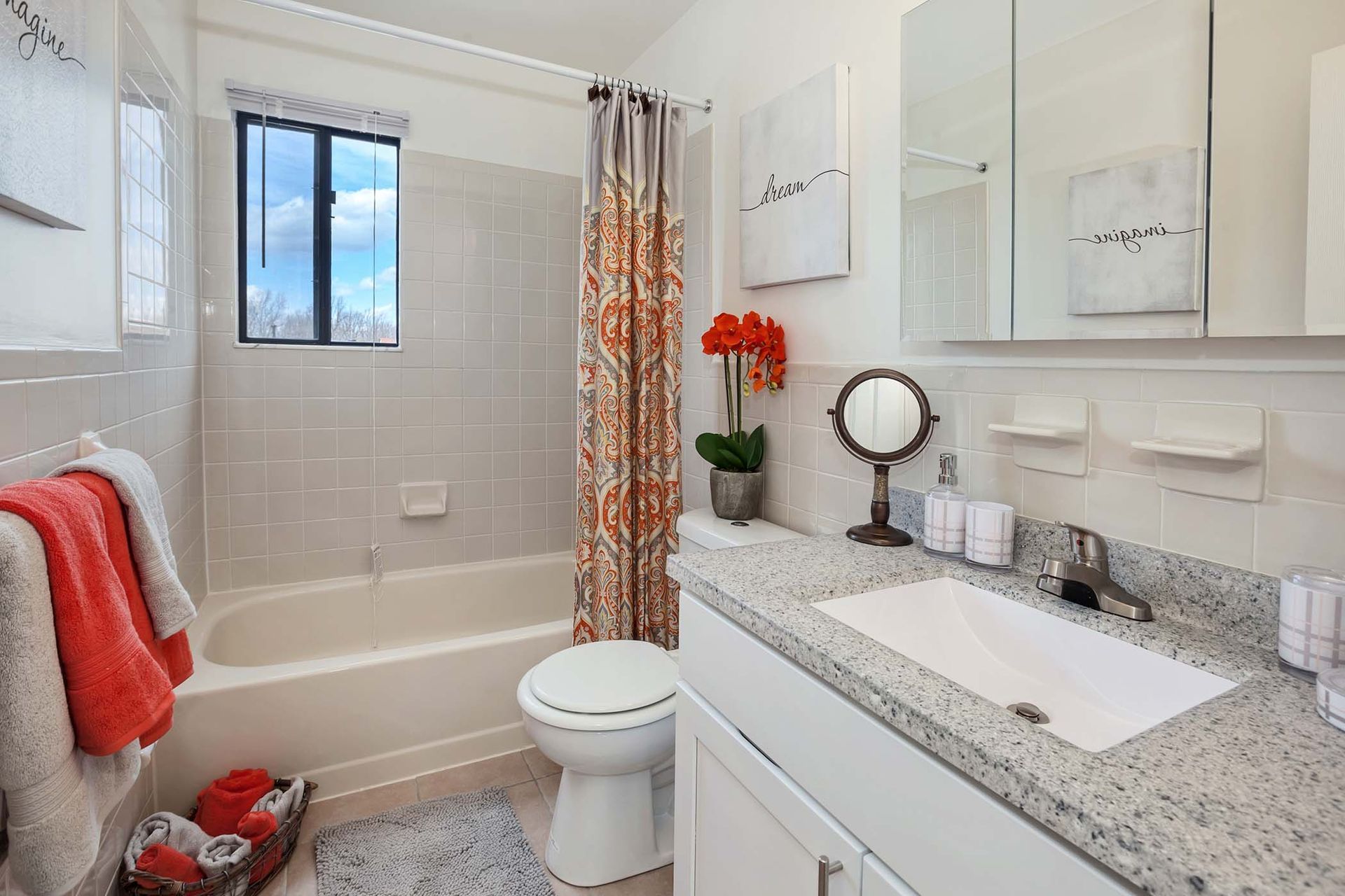 Bright apartment bathroom with a granite vanity, large mirror, and tub/shower.