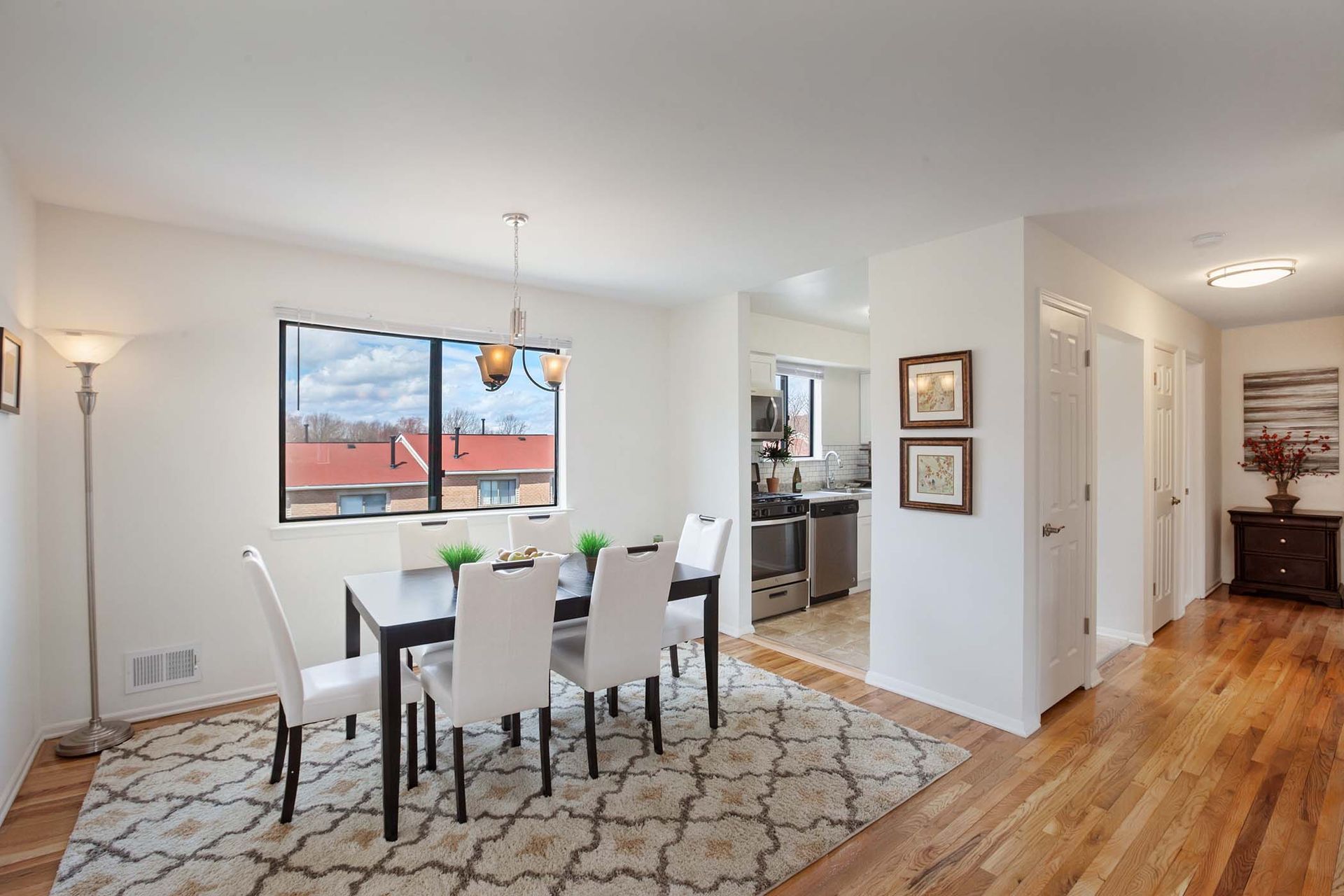Dining area in an apartment with a dark table, white chairs, and an open kitchen.