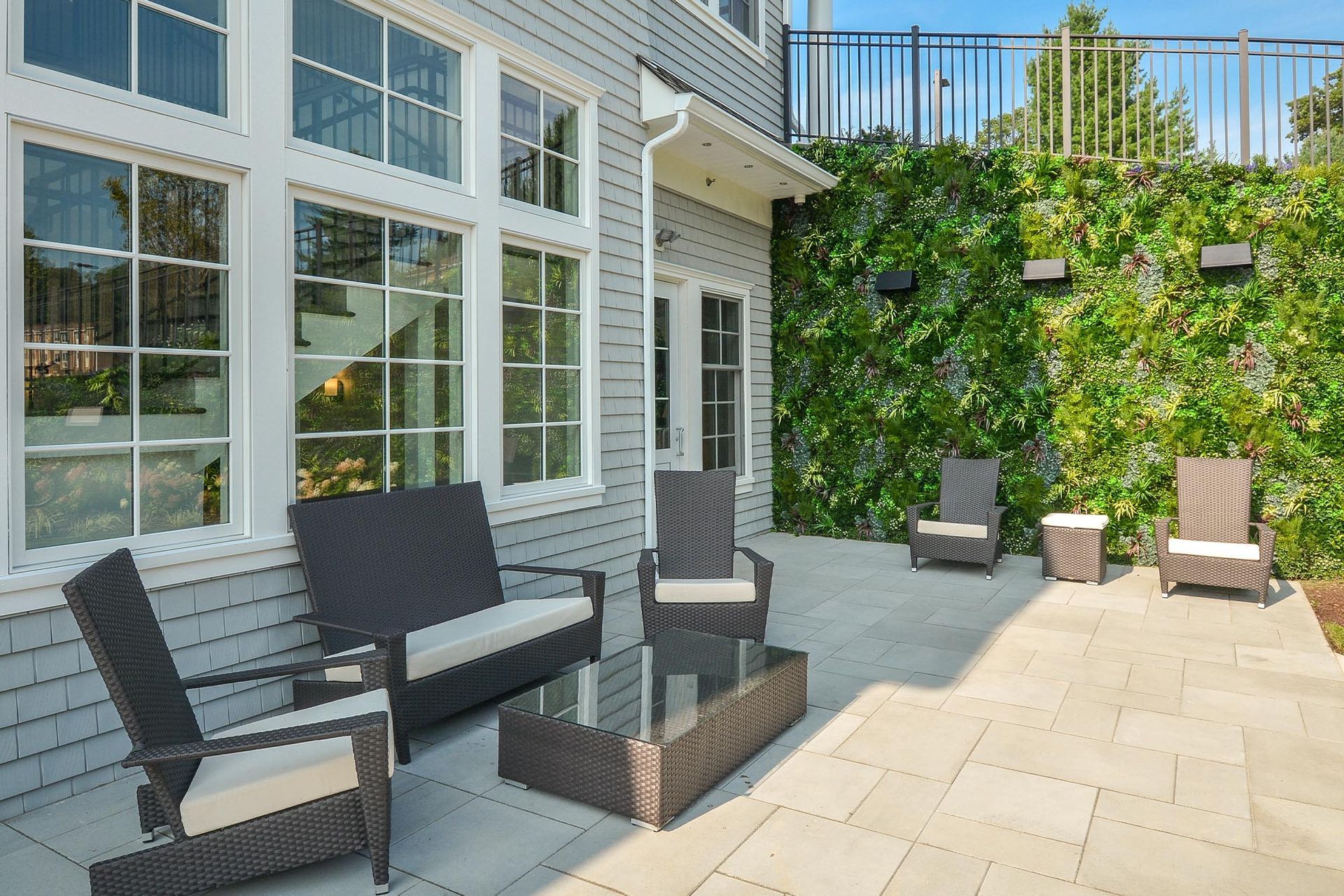 Outdoor communal patio with wicker seating and a glass coffee table beside a building wall.